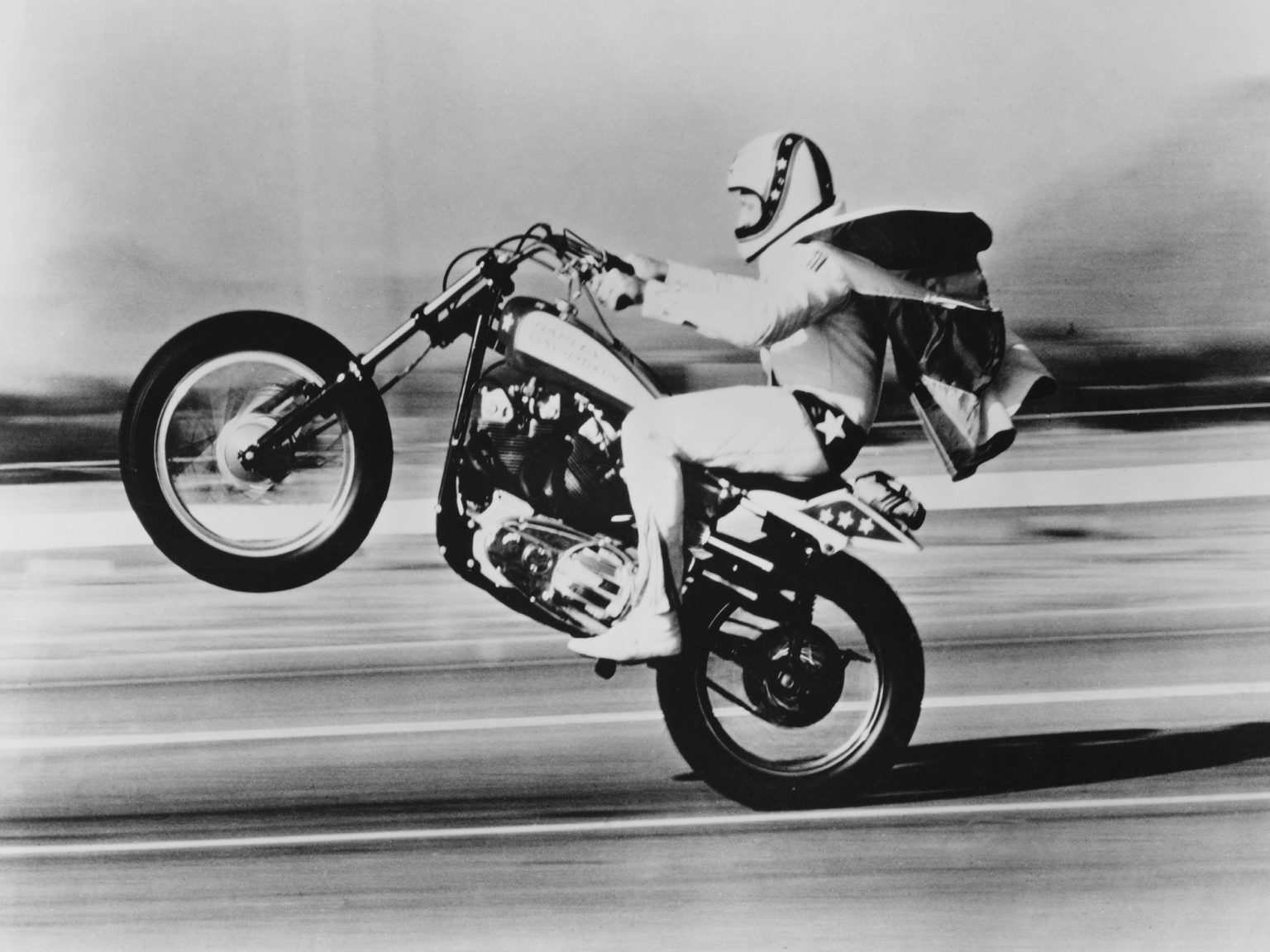 American stunt rider Evel Knievel (1938 - 2007) pulls a wheelie on his Harley Davidson motorcycle, circa 1975.